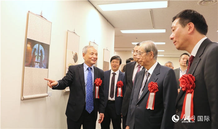 “湖州印象”攝影展主創(chuàng)、世界華人攝影協(xié)會副會長馮學(xué)敏向吳江浩大使、福田康夫前首相等嘉賓介紹展出作品。（人民網(wǎng) 許可攝）