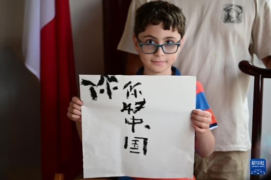 7月4日，在馬耳他桑塔露琪亞市的中國(guó)古典園林“靜園”，一名男孩展示他的書(shū)法作品。新華社發(fā)（喬納森·博格 攝）