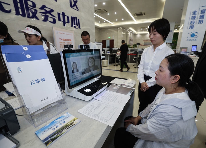 在浙江省嘉興市秀洲區(qū)王江涇鎮(zhèn)便民服務(wù)中心的“跨域通辦·云綜窗”窗口，辦理開業(yè)登記的個(gè)體工商戶（右一）通過(guò)該系統(tǒng)與江蘇省蘇州市吳江區(qū)盛澤鎮(zhèn)行政審批局工作人員視頻連線，進(jìn)行身份讀取及材料線上審核（2024年5月9日攝）。新華社記者 徐昱 攝