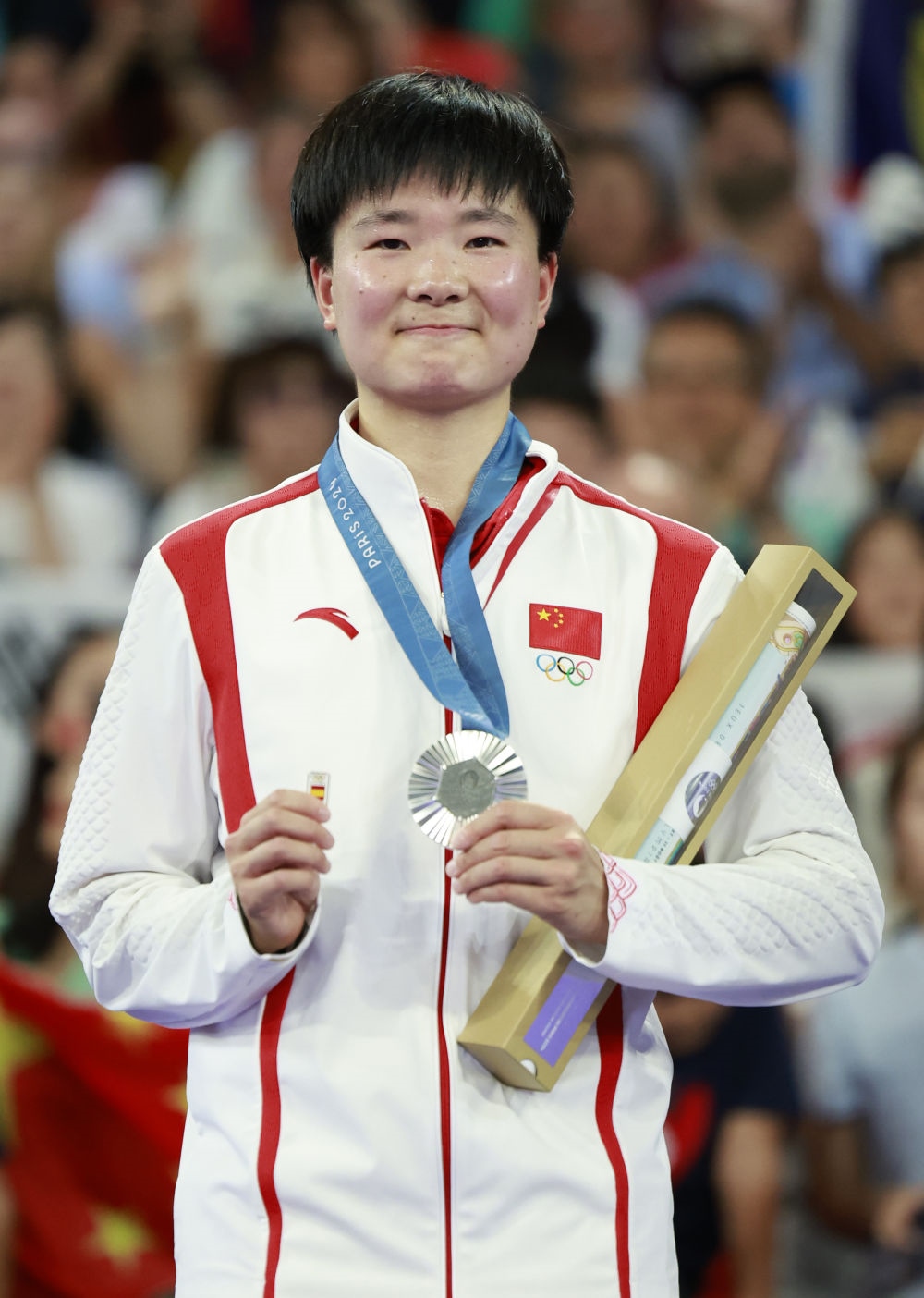 巴黎奧運(yùn)會羽毛球女子單打亞軍、中國選手何冰嬌在頒獎儀式上一手握著銀牌，一手握著西班牙奧委會徽章（2024年8月5日攝）。新華社記者 任正來 攝
