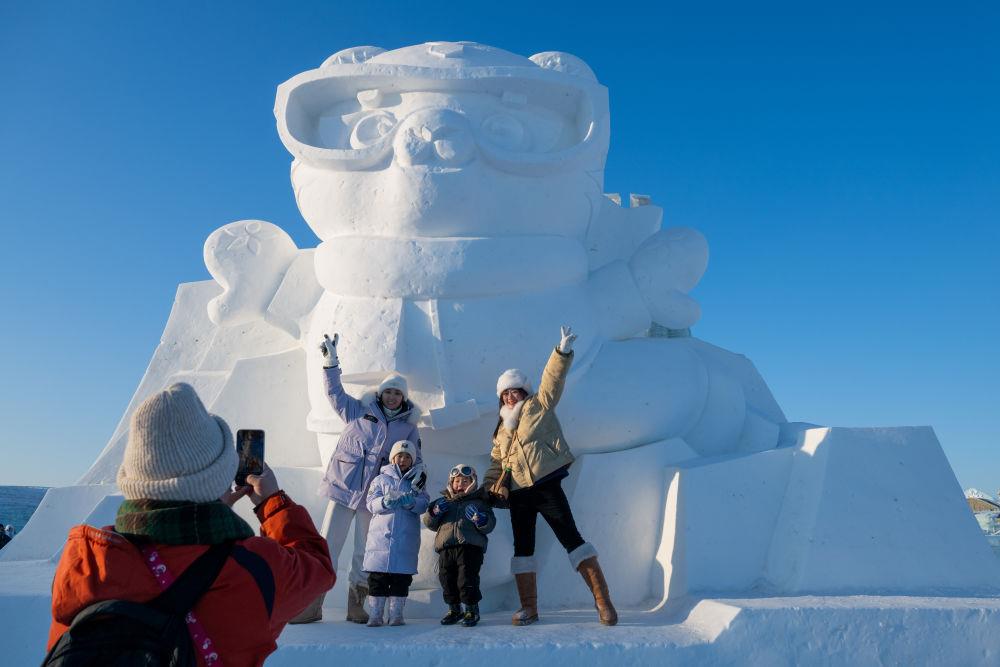 2025年1月3日，在黑龍江哈爾濱冰雪大世界園區(qū)，游客與亞冬會(huì)吉祥物雪雕“濱濱”合影